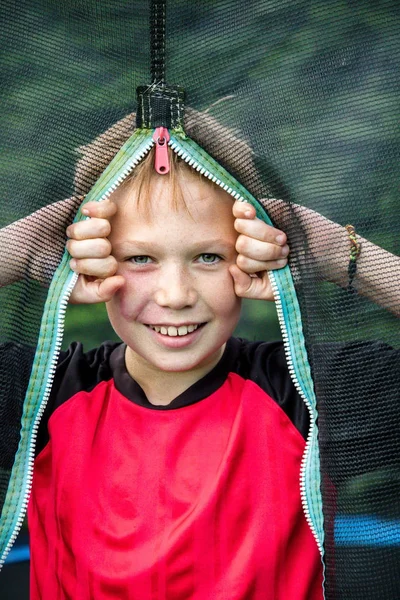 Cheeky pre-teen boy looking through trampoline net — Stock Photo, Image