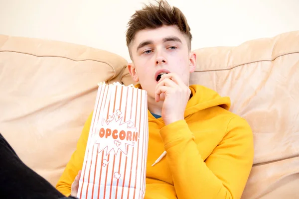 Tiener op een sofa eten popcorn — Stockfoto