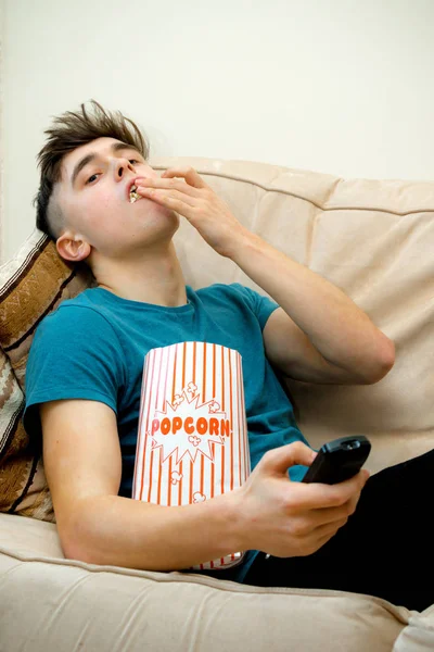 Tiener op een sofa eten popcorn — Stockfoto