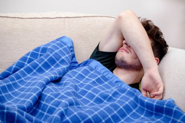 Kanepede uyuyan genç bir adam, battaniyeli.