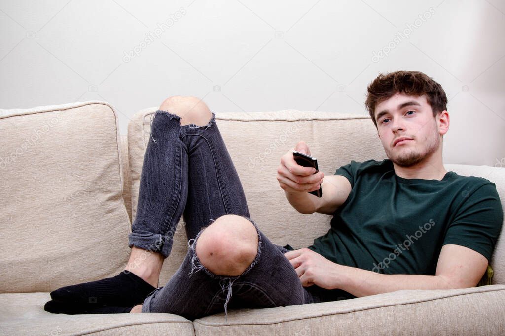 A young adult man using a remote control while on a sofa
