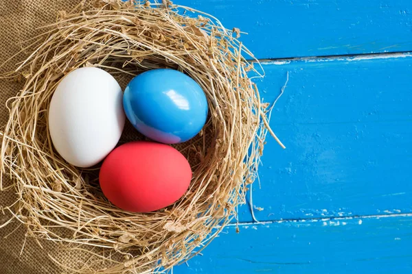 Piros, kék, fehér tojás (mint néhány ország zászlaja) fészek rusztikus, fából készült háttér, szelektív összpontosít, kép. Boldog húsvéti üdvözlőlap - hely a szöveg. — Stock Fotó