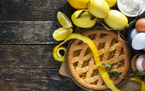 Вкусный лимонный пирог с кулинарными ингредиентами на деревянном столе — стоковое фото