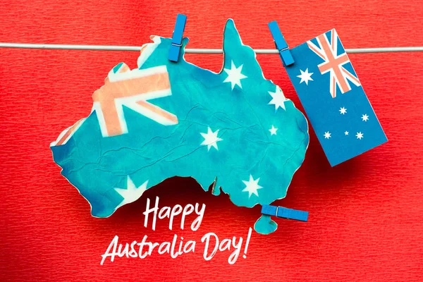 庆祝澳大利亚天假日在1月26日与愉快的澳洲天消息问候卡片横跨澳大利亚地图和旗子垂悬的钉子在蓝色背景 — 图库照片