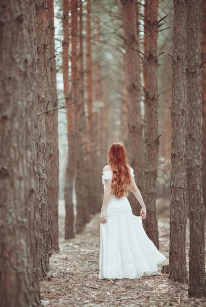 Ginger girl in white dress walking in pine forest. — Stock Photo, Image