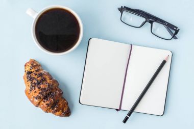 Mavi ofis Masaları boş not defteri, kalem, gözlük, taze kruvasan ve kahve fincanı. Metin için yer kopyalayın. Düz yatıyordu. Üstten Görünüm.