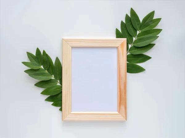 Empty wooden photo frame mock-up with green leaves around, isolated on white background. — Stock Photo, Image