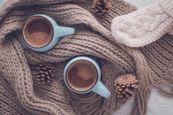 Noël et Nouvel An composition de vacances confortable avec écharpe, mitaines, cône de pin, tasses avec du cacao ou du chocolat sur le fond de béton gris. Couché plat, vue du dessus . — Photo