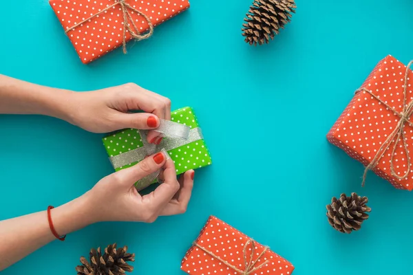 Новорічна та різдвяна святкова композиція з подарунковими коробками, сосновим конусом, жіночими руками упаковують подарунок на синьому фоні. Вид зверху, плоска лежала. Копіспазмі . — стокове фото