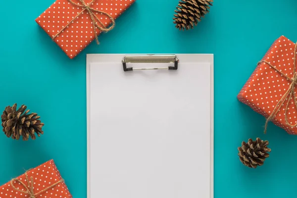 Christmas and New Year holiday to do list with notepad, gift boxes, pine cone on the blue background. Mock up. Flat lay, top view.