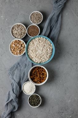 Ev yapımı granola yemek pişirmek için malzemeler: yulaf ezmesi, Kuru üzüm, Hindistan cevizi cips, tatlım, fıstık, kakao, yaban mersini, bitkisel yağ, keten, susam, kabak ve ayçiçeği tohumu. Beton arka plan. Üstten Görünüm.