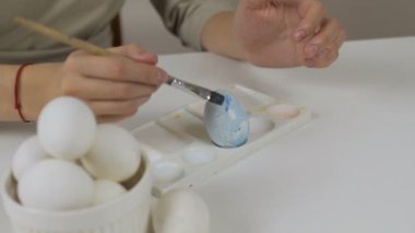 Tanınmayan kadın bir fırça ile Paskalya yumurtaları boyar. Bir bardak su ve yumurta bir kase tablodur. Tatil için hazırlanıyor.