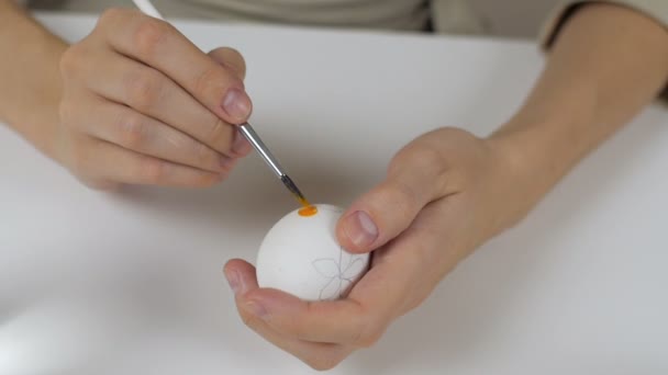 Femme méconnaissable peint des œufs de Pâques avec un pinceau. Sur la table il y a un verre d'eau et un bol d'œufs. Se préparer pour les vacances . — Video