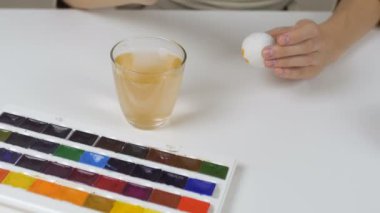 Tanınmayan kadın bir fırça ile Paskalya yumurtaları boyar. Bir bardak su ve yumurta bir kase tablodur. Tatil için hazırlanıyor.