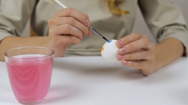 Tanınmayan kadın bir fırça ile Paskalya yumurtaları boyar. Bir bardak su ve yumurta bir kase tablodur. Tatil için hazırlanıyor.