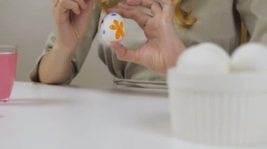 Tanınmayan kadın bir fırça ile Paskalya yumurtaları boyar. Bir bardak su ve yumurta bir kase tablodur. Tatil için hazırlanıyor.