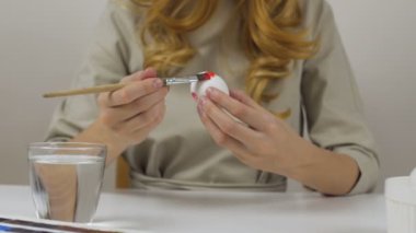 Tanınmayan kadın bir fırça ile Paskalya yumurtaları boyar. Bir bardak su ve yumurta bir kase tablodur. Tatil için hazırlanıyor.