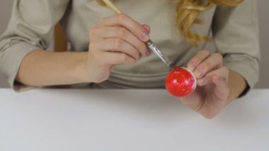 Tanınmayan kadın bir fırça ile Paskalya yumurtaları boyar. Bir bardak su ve yumurta bir kase tablodur. Tatil için hazırlanıyor.