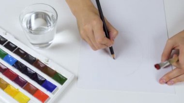 Tanınmayan kadın kalem eskiz kağıt Paskalya kartı üzerinde çizer. Bir palet boya ve bir bardak su ile geçerli.