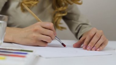 Tanınmayan kadın bir kroki bir Paskalya kartı için kağıt üzerinde parlak renklerle boyar. Bir palet boya ve bir bardak su ile geçerli.