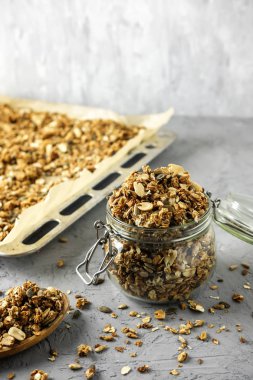 Ev yapımı granola depolama işlemi. Bir cam kavanoz, tahta kaşık ve bir fırın tepsisi beton zemin üzerine kuru bir kahvaltı ile.
