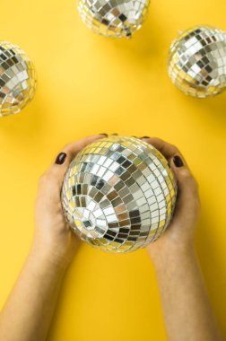 Kadın elleri, parlak sarı arka planda disko aynalı top şeklinde Noel oyuncağını düzgünce tutuyor. Yukarıdan bak. Düz yatıyordu. Mesaj için yer. Kopyalama alanı.