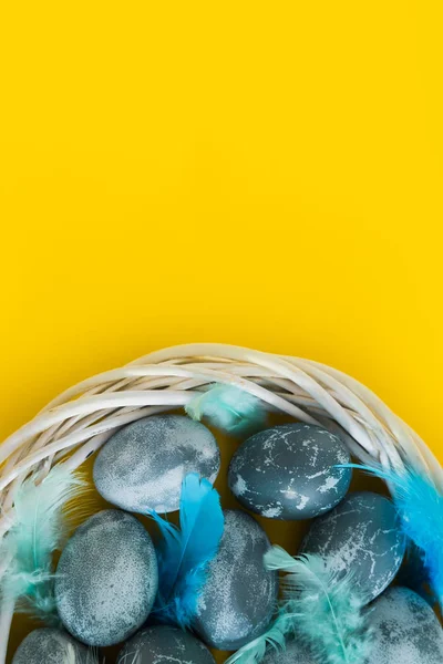 Blau strukturierte farbige Ostereier mit Vogelfedern in einem Nest oder Kranz auf einem leuchtend gelben Feiertagshintergrund. Frühjahrsferienkonzept. Kopierraum. Flach lag er. Ansicht von oben. — Stockfoto