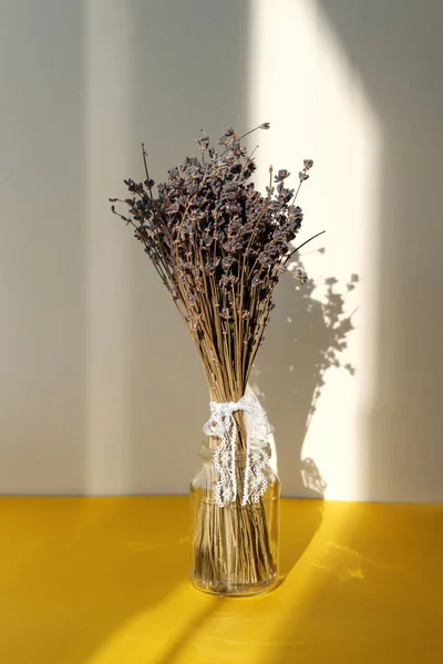 Bouquet of purple lavender in glass jar on bright yellow background. Hard light falls on still life with flowers. — Stock Photo, Image