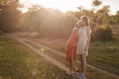 İki kız arkadaş gün batımında ormanda birlikte yürürler. Güzel bir yaz havası var. İkisi de elbise giymiş..