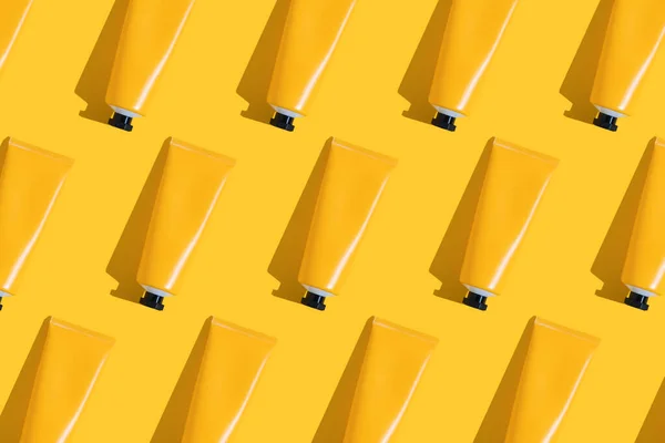 Patrón de tubos amarillos de protector solar sobre fondo amarillo brillante con sombra dura. Protección solar en verano . — Foto de Stock