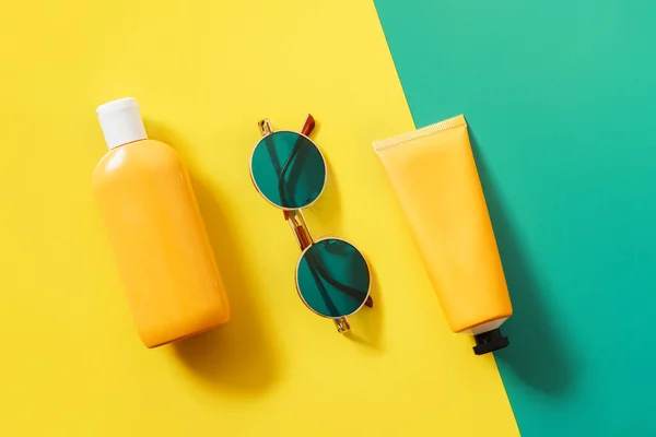 Summer bright flatlay on colorful background with tubes and bottle with sunscreen, green sunglasses. Hard shadows and light. Top view. Flat lay. Trend style. Copyspace.