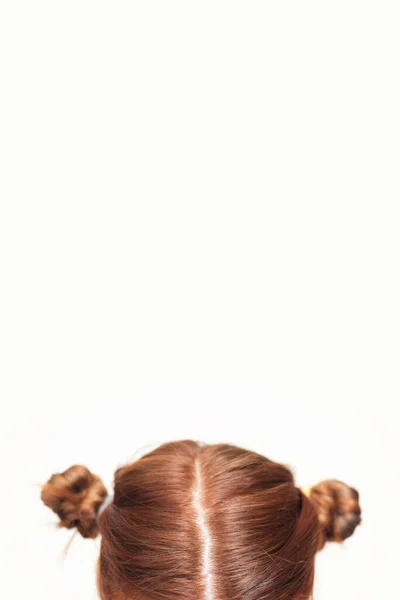 Cabeza de una chica con dos desordenados bollos de pelo rojo rizado retorcido sobre fondo blanco. Peinado creativo. Espacio de copia . — Foto de Stock