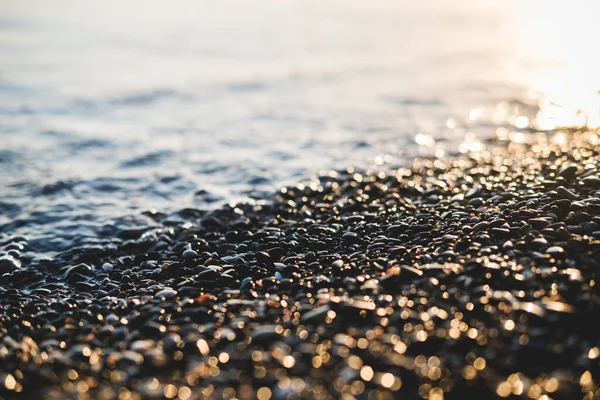 바다 옆에 있는 작은 돌들은 보케 효과가 있습니다. 은은 한 배경에 텍스트를 위한 장소입니다. 여름 벽지, 맑은 석양 빛. — 스톡 사진