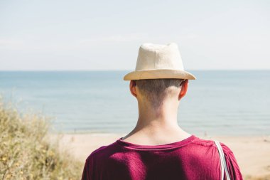 Şapkalı ve çantalı bilinmeyen genç adam deniz kıyısına gider..