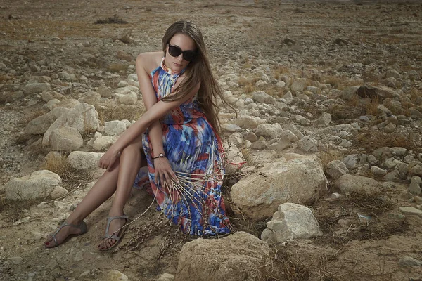 Modelo menina em um vestido bonito senta-se em uma rocha . — Fotografia de Stock