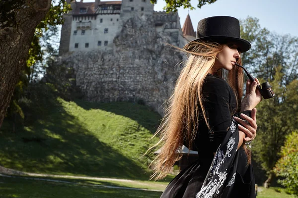 Modelo chica en un sombrero y vestido negro camina en el patio de th —  Fotos de Stock