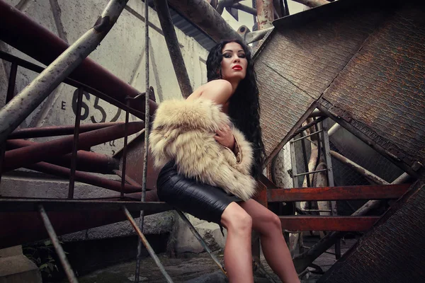 Menina bonita em casaco de pele posa no pátio da fábrica — Fotografia de Stock