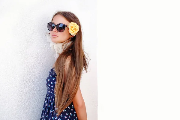 Modelo de niña en un sombrero y gafas de sol posando contra una pared blanca . — Foto de Stock