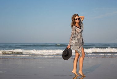 Güzel, zarif bir kız, modeli deniz kıyısı elini kolunu sallaya dönüyor. Can