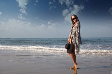 Güzel, zarif bir kız, modeli deniz kıyısı elini kolunu sallaya dönüyor. Can