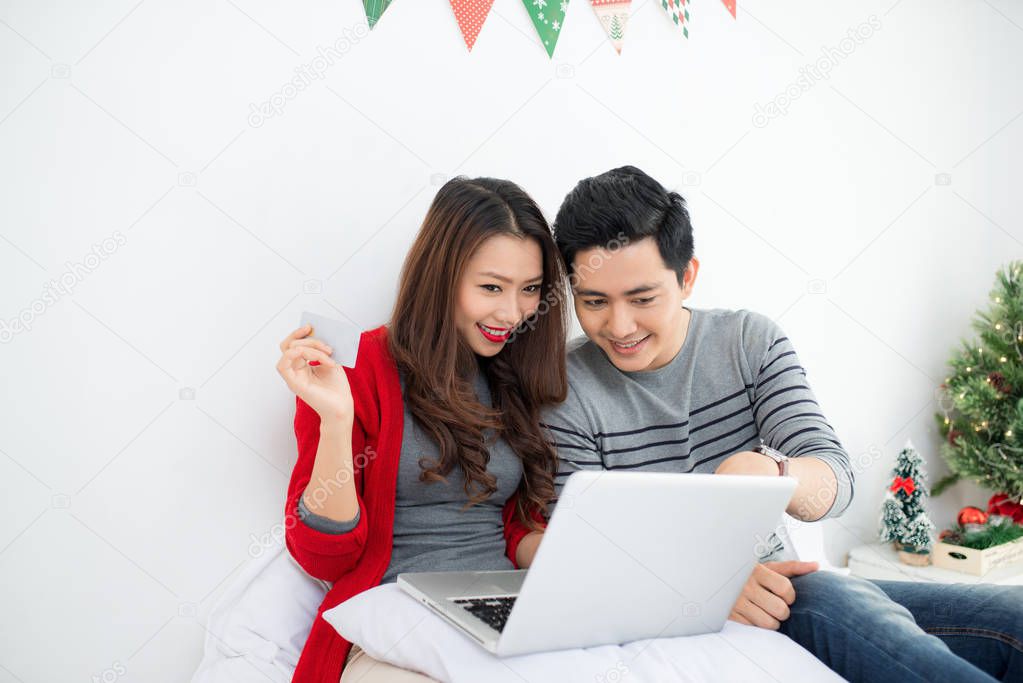 Christmas. Asian Couple Shopping Online at home celebrating New 