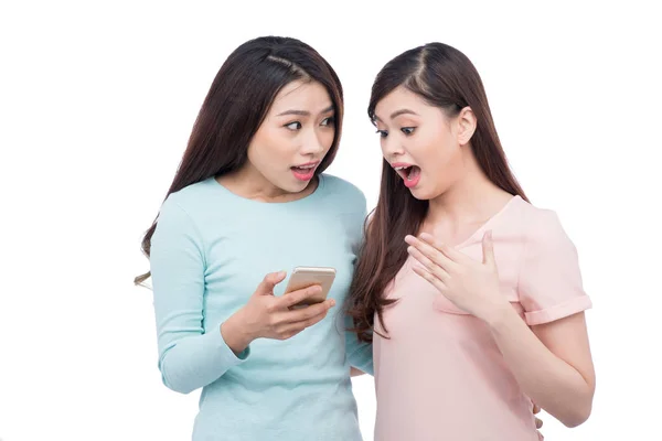 Две молодые девушки используют смартфон. Улыбающиеся юные подруги — стоковое фото