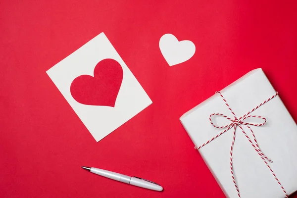 Handgemachte kleine Geschenkschachtel mit Herz-Symbol auf rotem Hintergrund. — Stockfoto