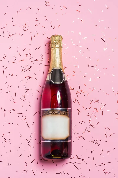 Kutlamanın düzleşmesi. Pembe arka planda renkli parti flamaları olan şampanya şişesi.. — Stok fotoğraf