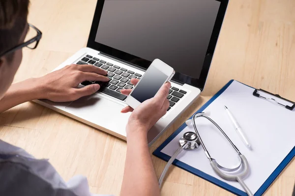 Doctor usando un ordenador portátil y un teléfono inteligente — Foto de Stock