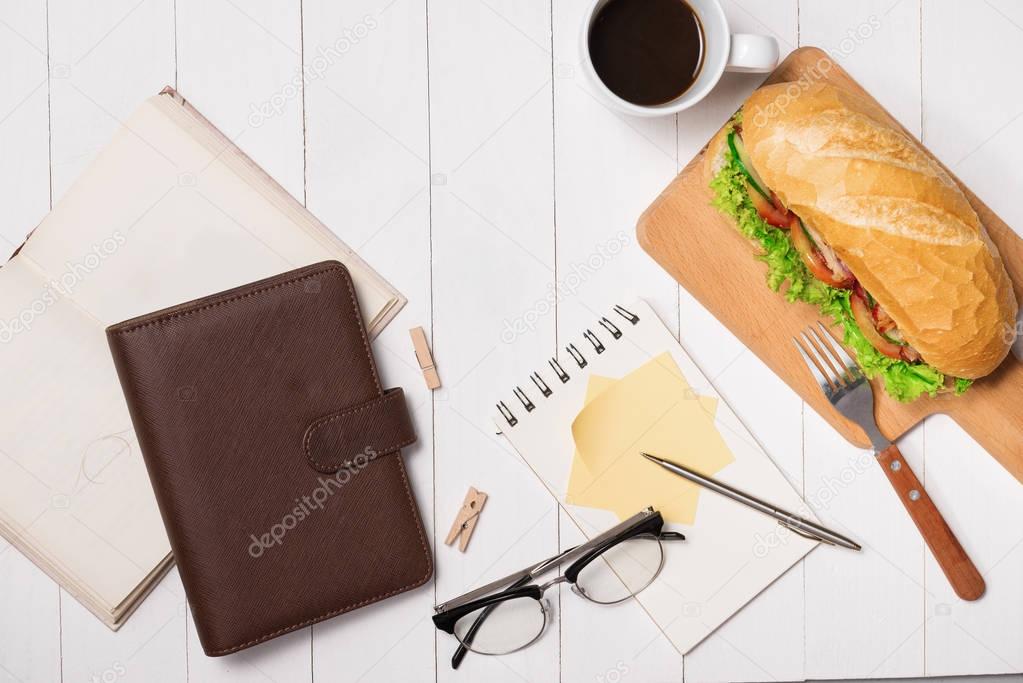 Snack at break time. Healthy business lunch in office, top view of Vietnamese sandwich, or Ban Mi on white wooden desk with coffee, mobile phone and notepad with pen flat lay.