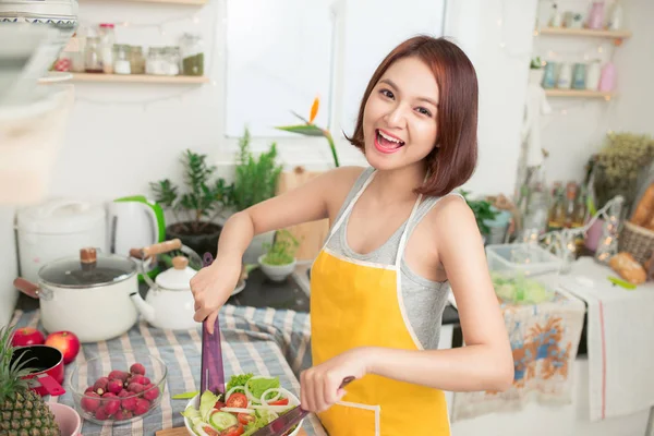 Fiatal ázsiai nő, ami salad, konyhában mosolyogva és nevetve boldog otthon. — Stock Fotó