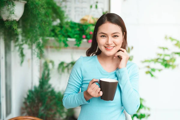 Retrato de una mujer asiática feliz pensando y sosteniendo café o taza de té en el desayuno —  Fotos de Stock