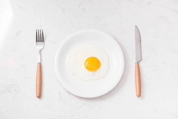 Fried egg on plate, fork and knife — Stock Photo, Image