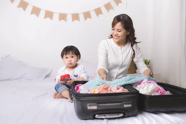 Asian mom and baby girl with suitcase baggage and clothes ready